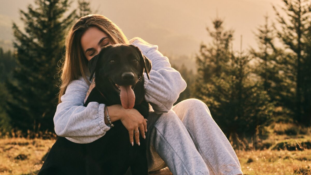 Woman,Embracing,Her,Black,Labrador,Retriever,In,A,Scenic,Mountain